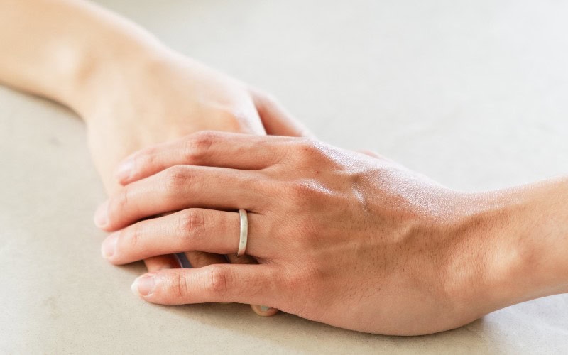 A man's hand with wedding ring holding a lady's hand